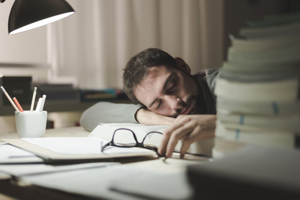 Opositor agotado descansando sobre libros tras largas horas de estudio preparando oposiciones